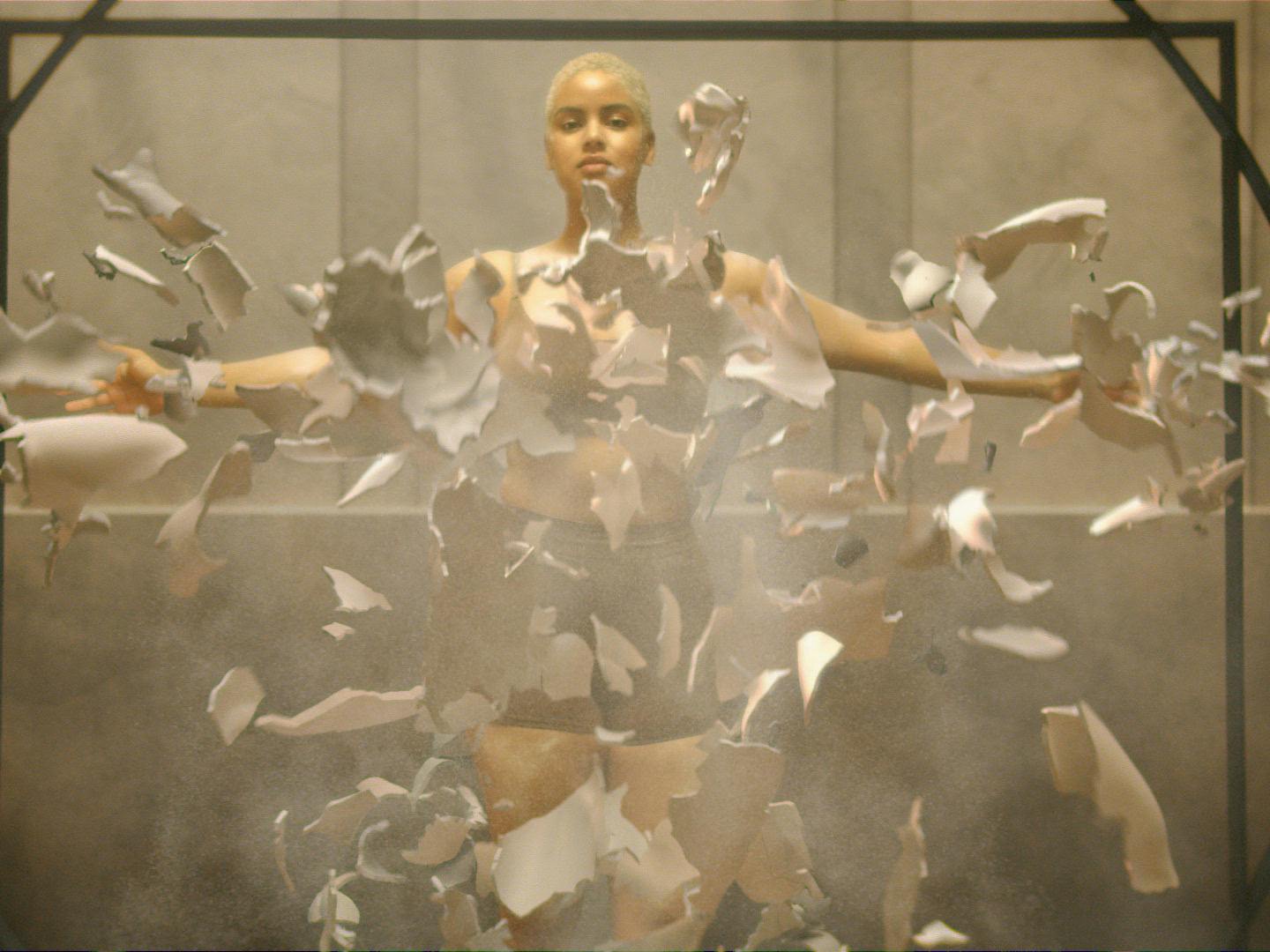A woman with short hair looking powerful with arms outstretched while pieces of a broken mold representing a historically male centric health research paradigm float around her.