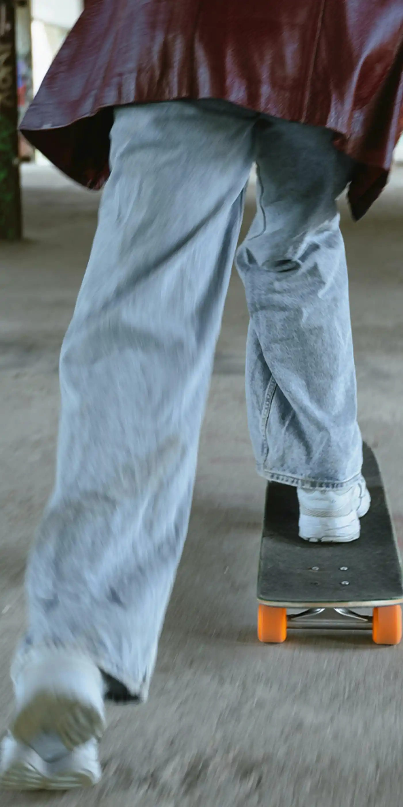 Person on a skateboard gliding away from camera through a graffiti-covered abandoned building with concrete pillars, wearing a maroon jacket and light jeans — representing the cultural momentum and forward motion at the heart of movement marketing strategy