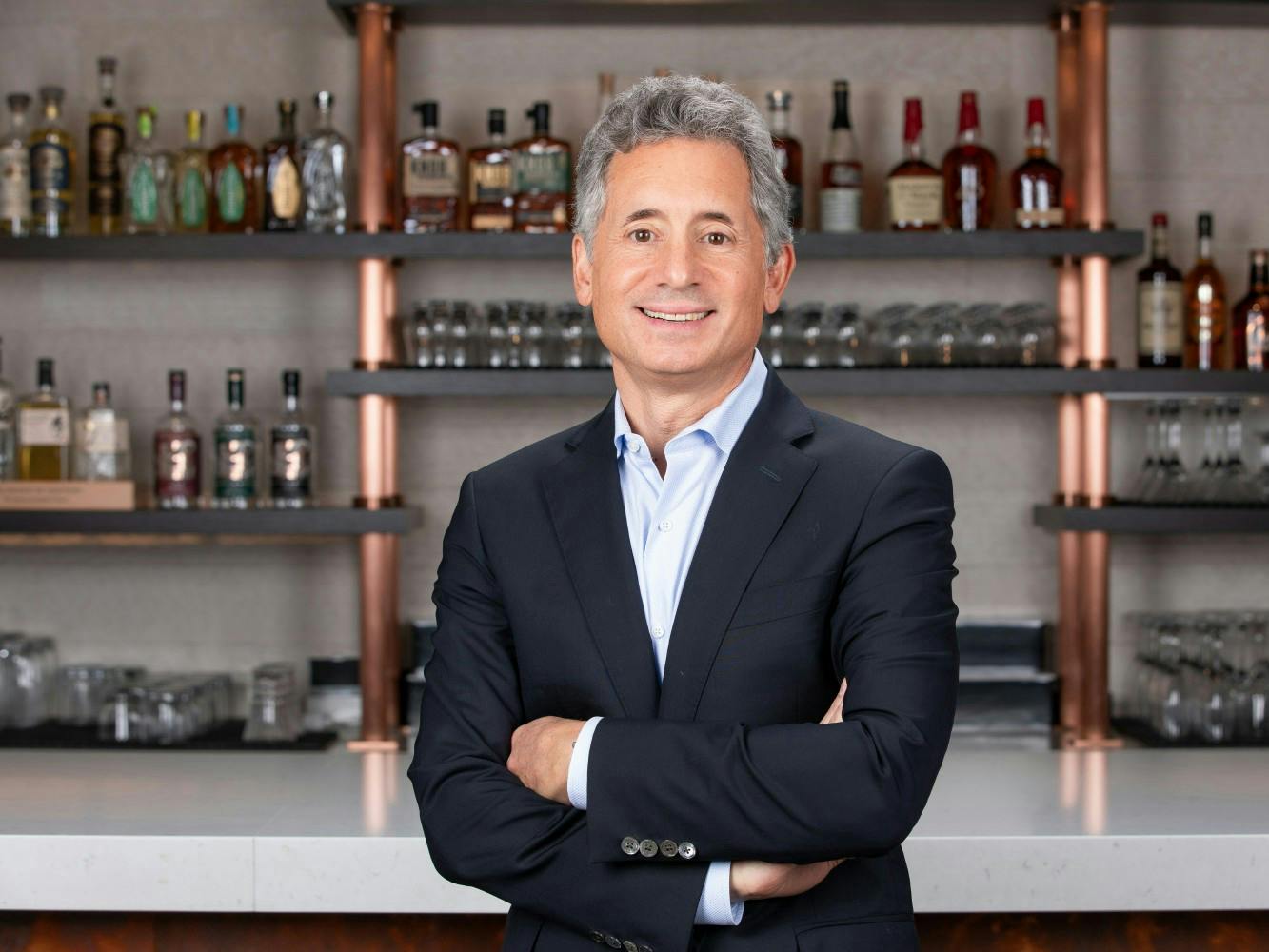 Portrait of Beam Suntory President and CEO Albert Baladi posing in front of a bar while wearing a suit.