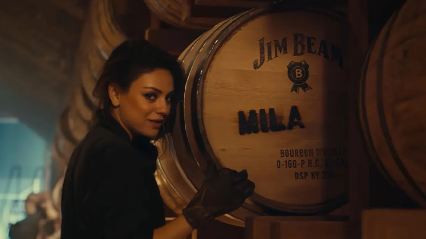 Actress Mila Kunis stands in front of a barrel of Jim Beam whiskey.