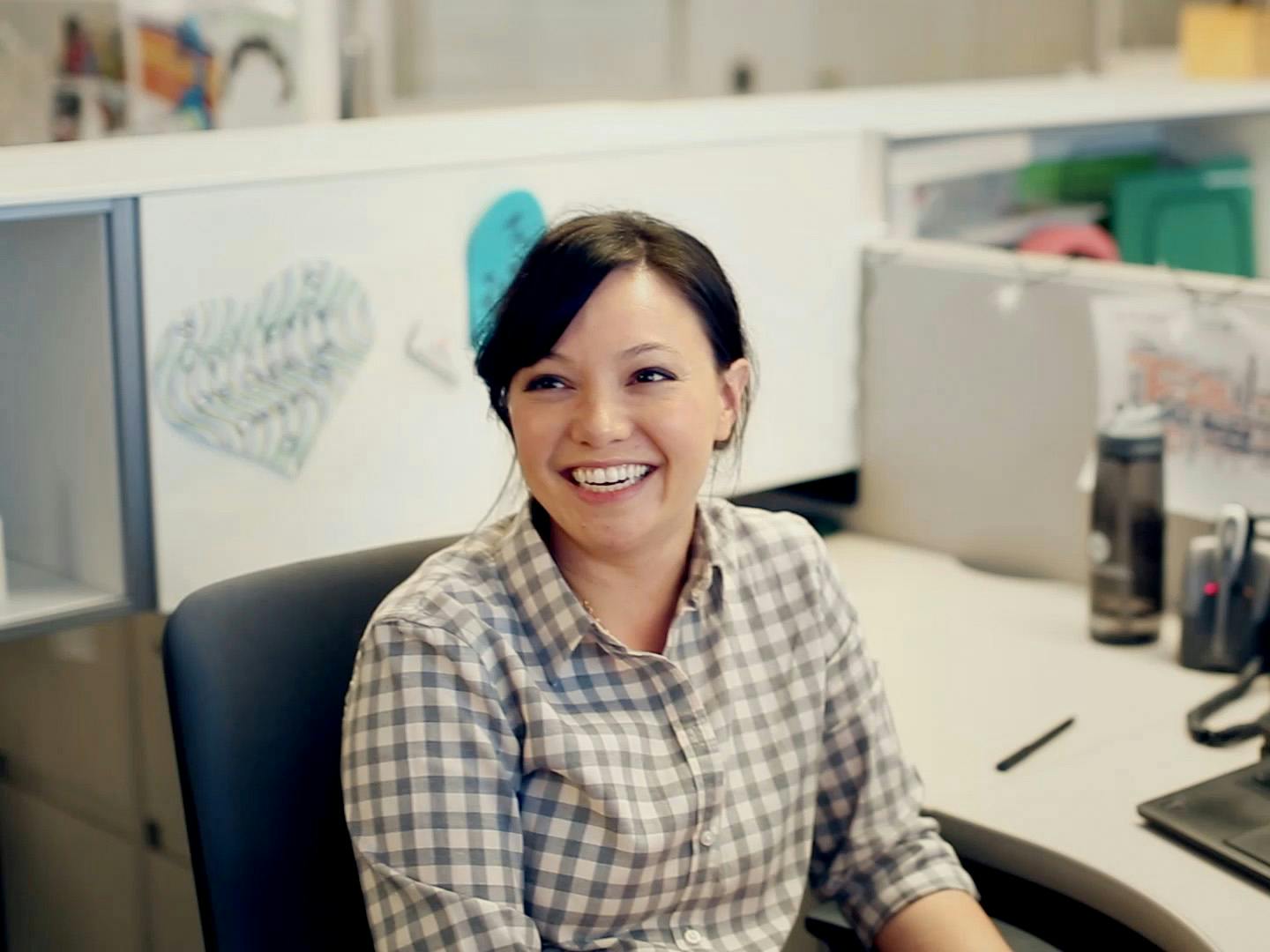 Woman wearing plaid with hair pulled back smiling with her mouth open at her work cubicle. Still from the “SunTrust Momentum OnUp” campaign.