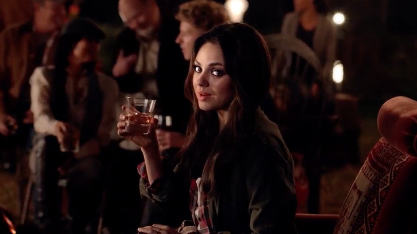 Actress Mila Kunis savors a glass of Jim Beam whiskey in a crowded room. 