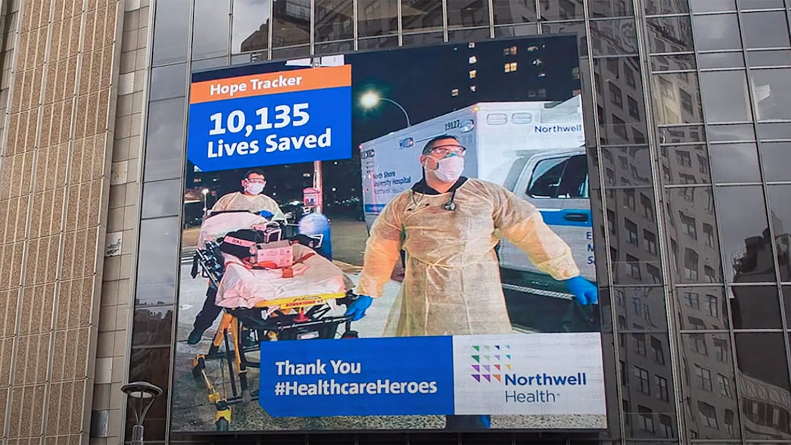A jumbotron featuring two male healthcare workers wearing head-to-toe PPE.