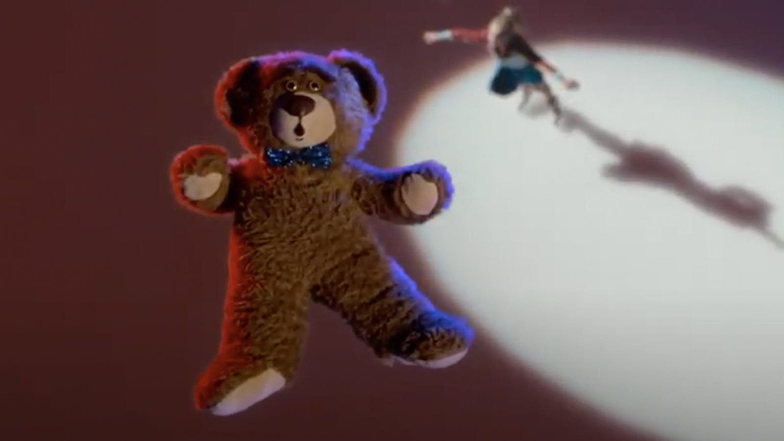 Screen grab of a teddy bear up in the air. A young girl can be seen in the distance. 