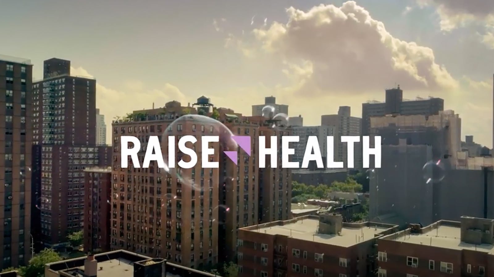 A city center landscape on a sunny day, with a bubble floating perfectly in the middle of the image. Text reads “Raise Health.”