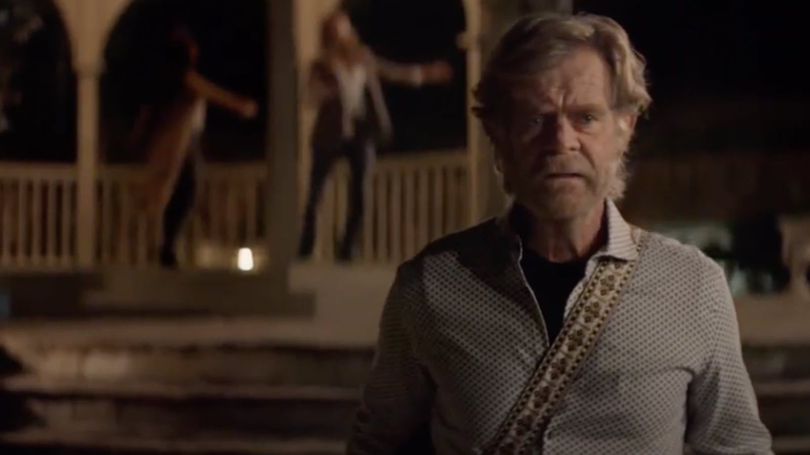 Actor William H. Macy wears a robe in the dark in front of a house as someone behind him calls his name.