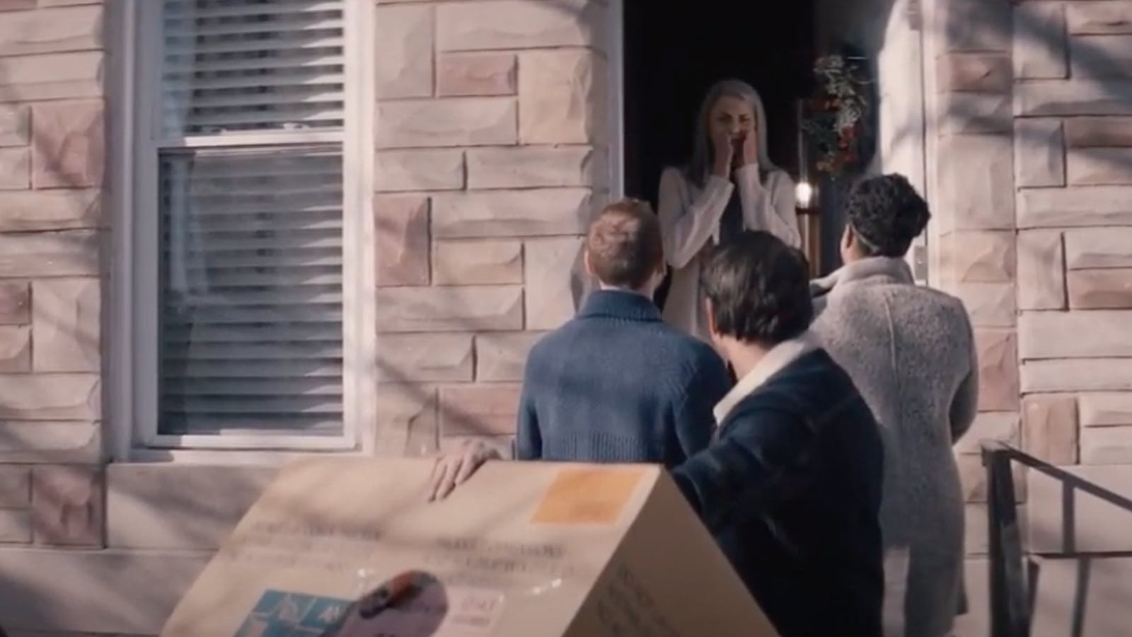 A surprised woman opens the door to find three guests in front of her home for the “Second Shift” LifeBridge campaign.