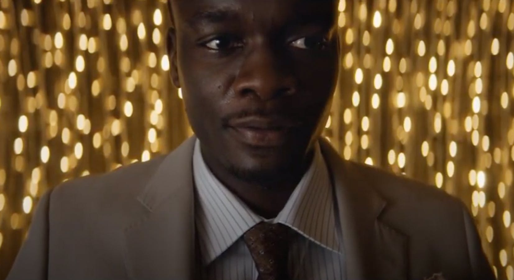 Close-up of a man wearing a suit, looking nervously to the side. In the background, twinkling lights. 