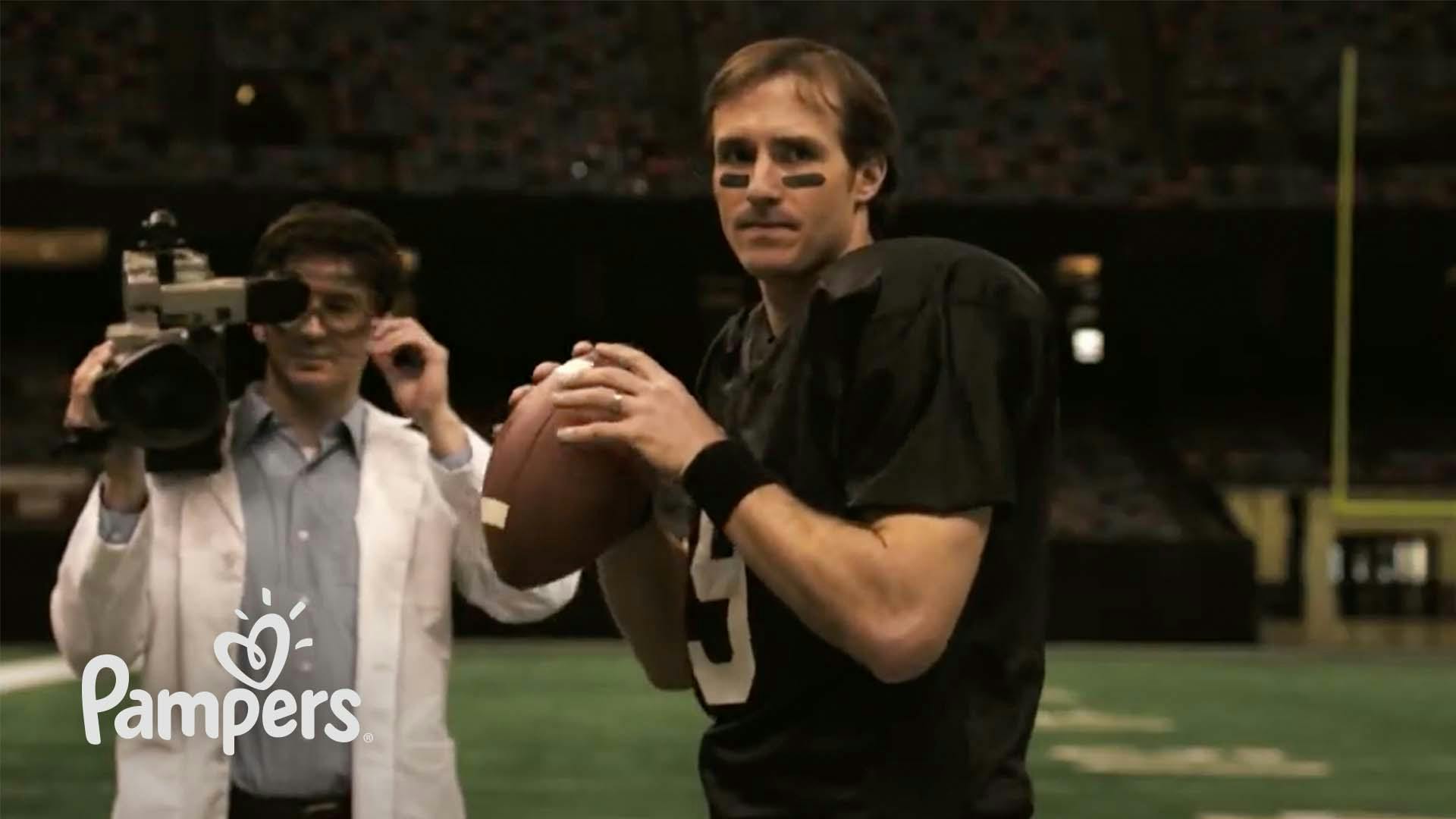 Quarterback Drew Brees holds the football while a man in a white lab coat with a video camera stands next to him.