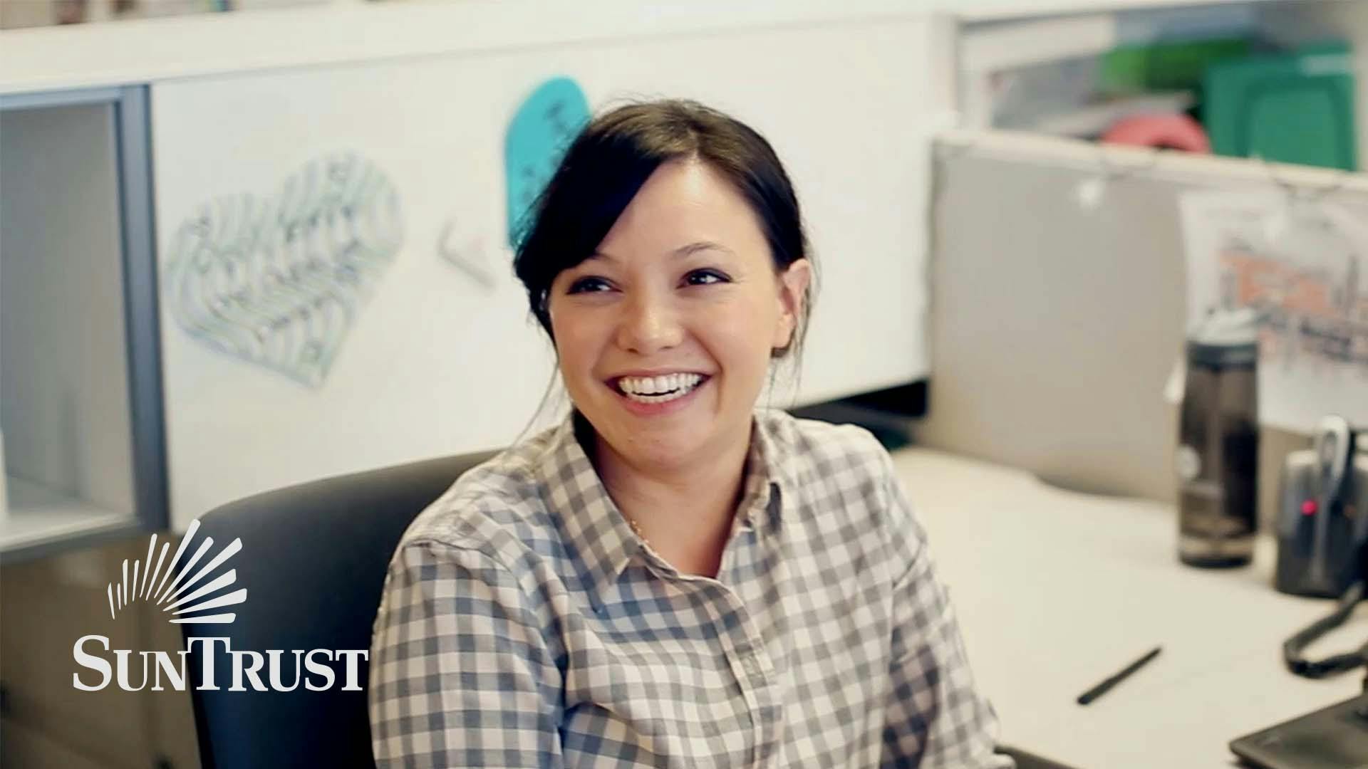 Woman wearing plaid with hair pulled back smiling with her mouth open at her work cubicle. Still from the “SunTrust Momentum OnUp” campaign.