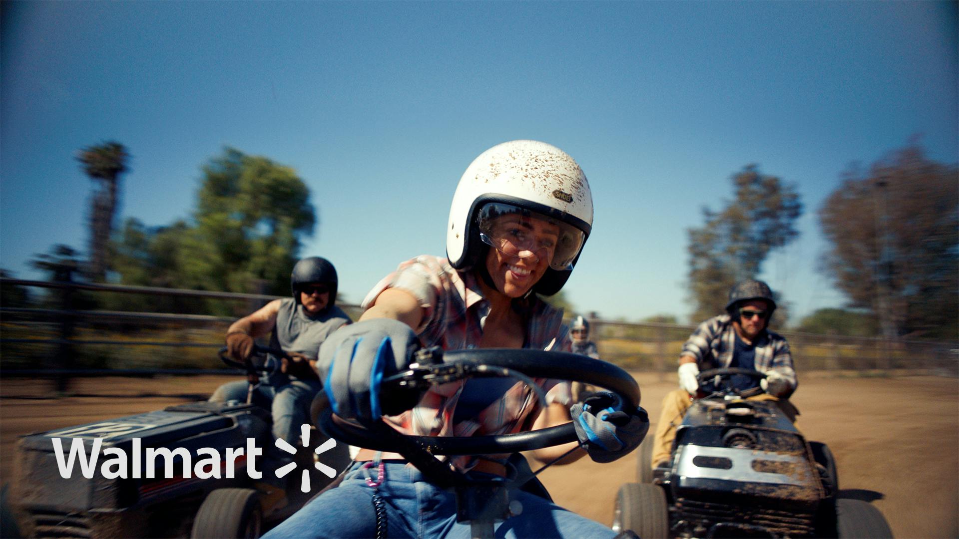 Still of a young woman wearing a helmet on a small tractor, racing two men in the “Better Living” Walmart commercial.