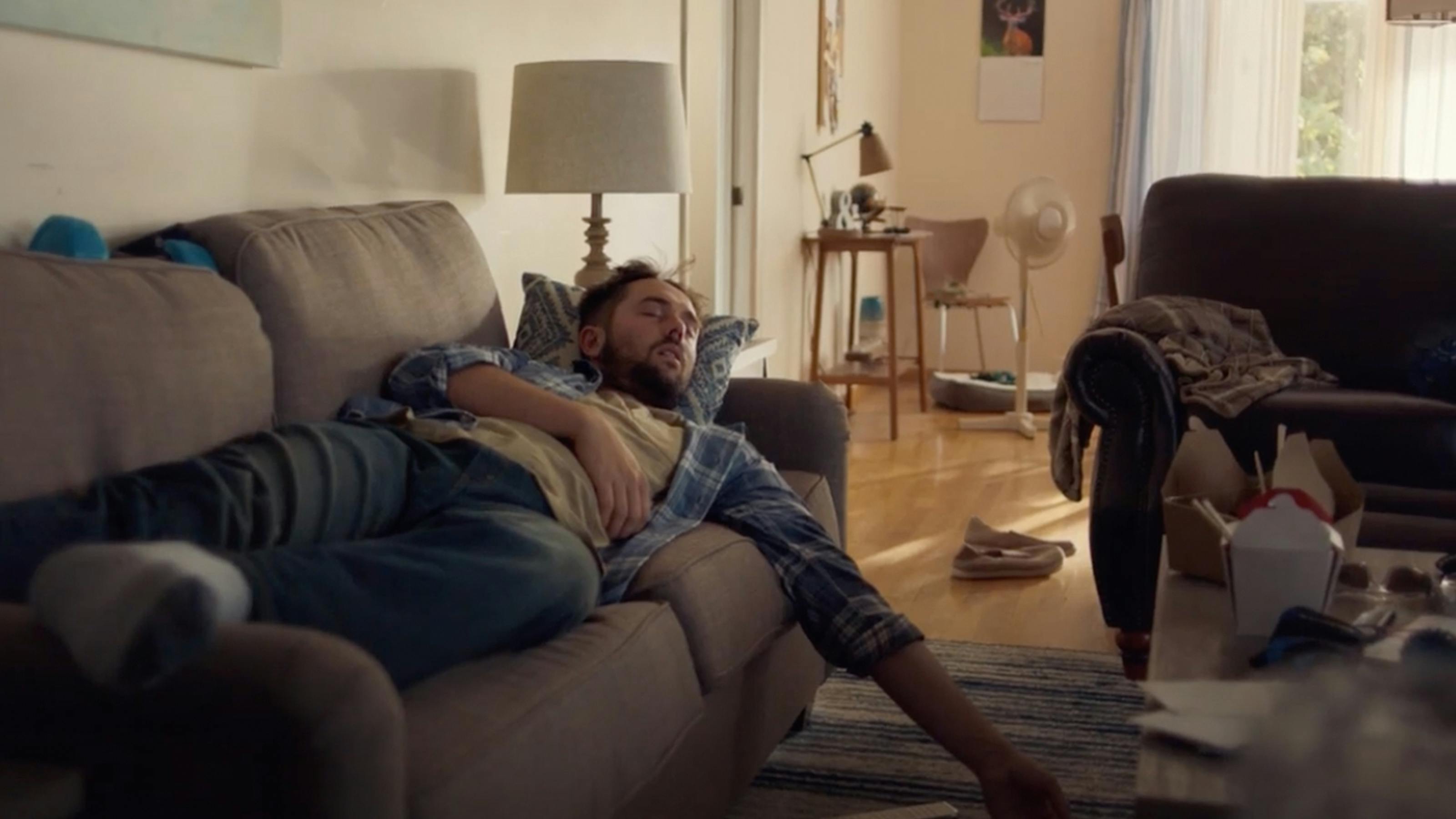 Screen grab of man napping on the couch in an untidy apartment for “Snore” Walmart campaign.
