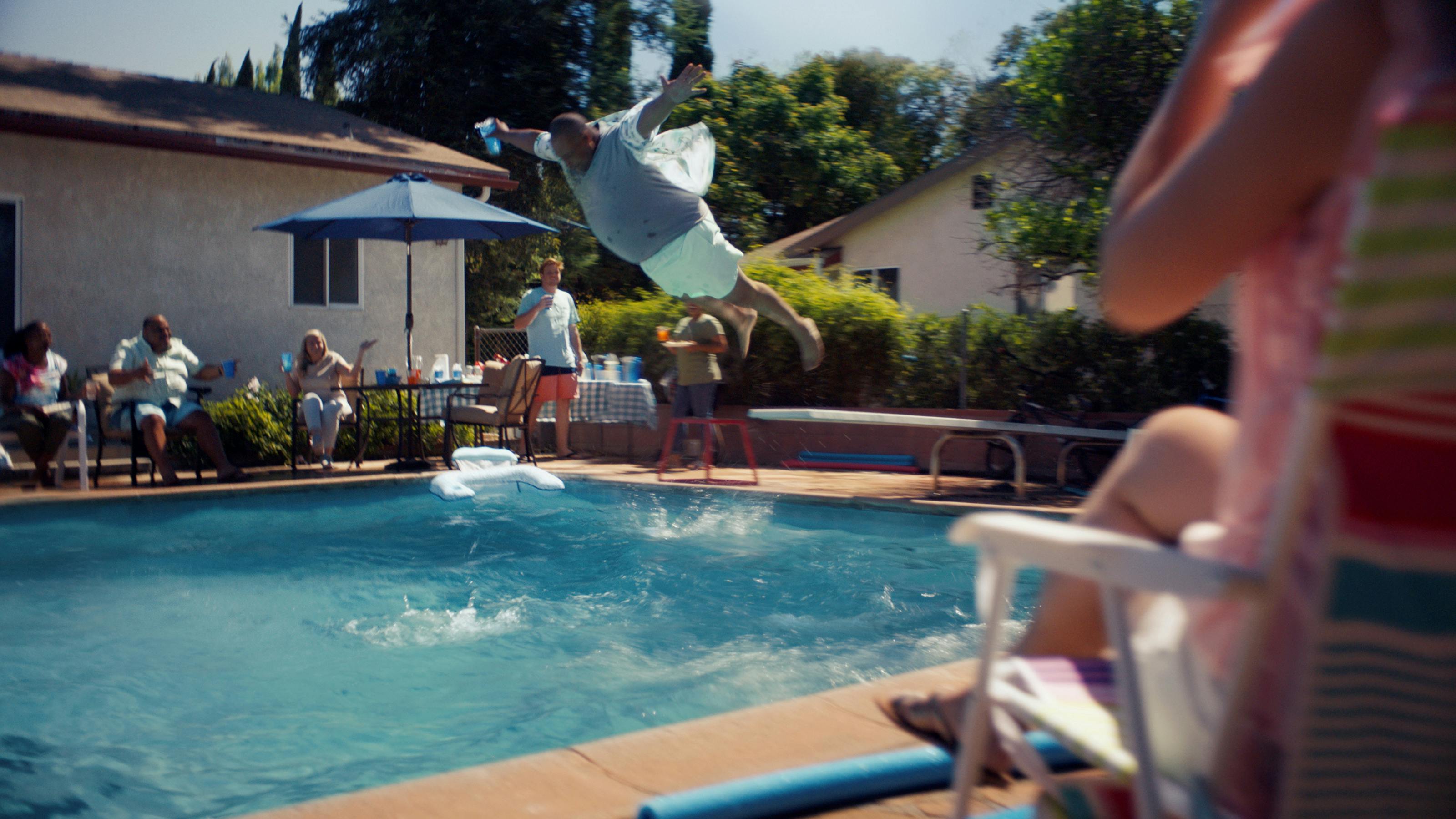 Screen grab of fully-clothed man caught mid-air as he plunges into the swimming pool while others look on.